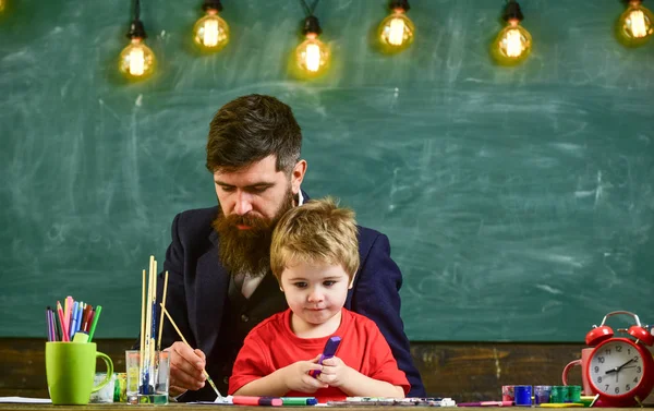 Öğretmen sakal, baba ve küçük oğul çizerken, sınıfta oluşturma, kara tahta arka plan ile. Çocuk ve resim, çizim meşgul yüzleri öğretmen. Çizim ders kavramı