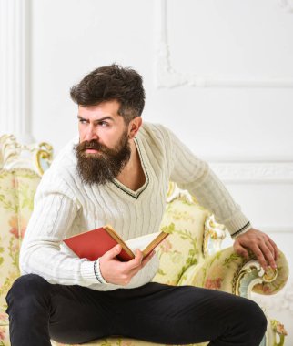 Sakal ve bıyık oturur barok tarzı kanepe, tutar kitap, beyaz duvar arka plan üzerinde olan adam. Edebiyat kavramı üzerine düşünceler. Maço katı yüz kitap okumayı yeni bitirdim. Adam edebiyat hakkında düşünme