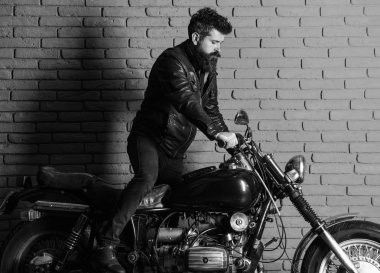 adam bir motosiklet. Yenilikçi, vahşi Motorcu deri ceket ciddi yüzüne üzerinde motosiklet üzerinde alır. Sakallı, motorcu motorlu bisiklet garaj, tuğla duvar arka plan yakınındaki deri ceketli adam.