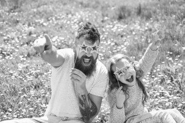 Rock yıldız kavramı. Baba ve kızı, grassplot, arka planı yeşil çimenlerin üzerinde oturur. Aile açık havada eğlence harcamak. Çocuk ve yıldız şekilli eyeglases photo booth özniteliğine çayır ile poz baba