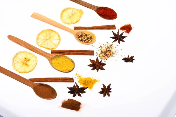 Composition of spoons with spices and dried oranges. Spoons filled with kitchen herbs and spices. Culinary art concept. Spoons with spices as red pepper, curcuma and cinnamon on white background