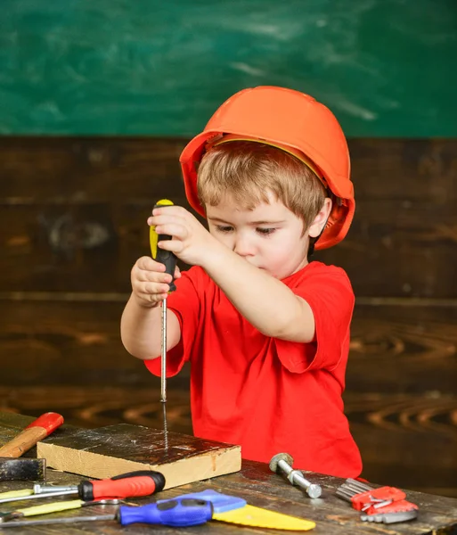 Kid boy segura ferramenta de chave de fenda. Criança na cara ocupada brinca com chave de fenda na oficina. Criança no capacete bonito jogando como construtor ou reparador, ou artesanato. Conceito de artesanato e oficina — Fotografia de Stock