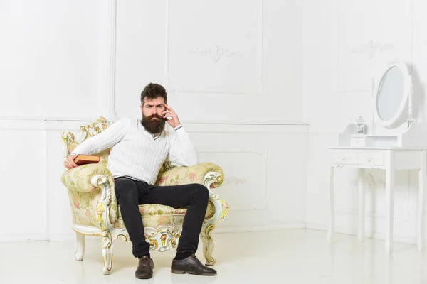 Conférencier assis sur un fauteuil et tient livre, fond de mur blanc. Scientifique, professeur sur le visage réfléchi analysant la littérature. L'homme à la barbe et à la moustache passe ses loisirs avec le livre. Concept intelligent — Photo