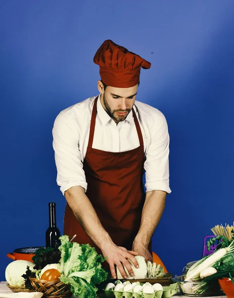 Koch mit geschäftigem Gesicht hackt Kohl mit Messer auf blau — Stockfoto