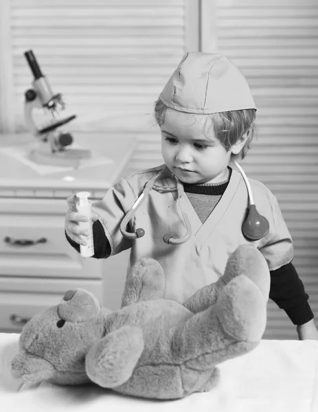 Pediatra niño en uniforme quirúrgico sostiene jeringa sobre fondo de madera . — Foto de Stock