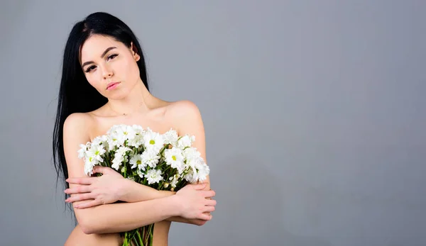 Mujer escondiendo sus pechos, cubre con ramo. Cáncer de mama. Señora cubre los pechos con flores, fondo gris. Chica en la cara tranquila desnuda sostiene flores de manzanilla en frente del pecho — Foto de Stock