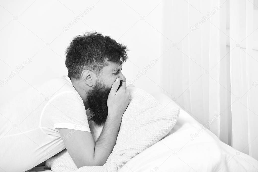 Man in shirt laying on bed, white wall on background. Nap and siesta concept. Macho with beard and mustache yawning, relaxing, having nap, rest. Guy on sleepy tired face yawning