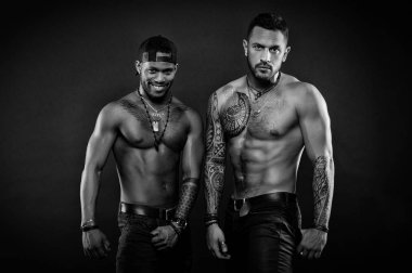 Machos with muscular tattooed torsos look attractive, dark background. Athletes on confident faces with nude muscular chests. Masculinity concept. Guys sportsmen with sexy muscular torsos clipart