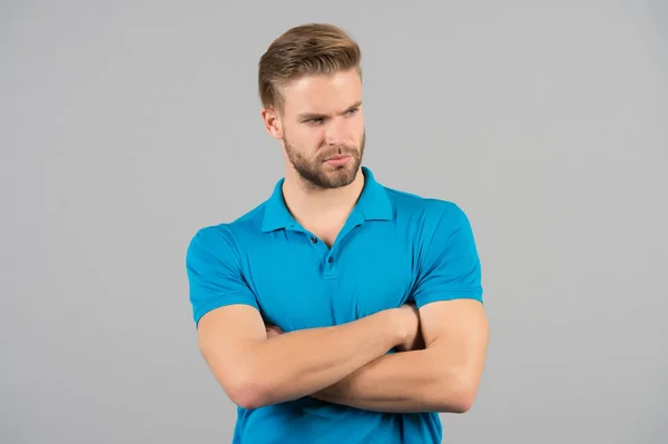 Człowiek ścisłego wątpliwy twarz pozowanie pewnie z składany skrzyżowane ręce na klatce piersiowej, szare tło. Człowiek wygląda atrakcyjnie w casual shirt niebieski. Facet Brodaty nosi atrakcyjny dorywczo koszulę. Koncepcja moda — Zdjęcie stockowe