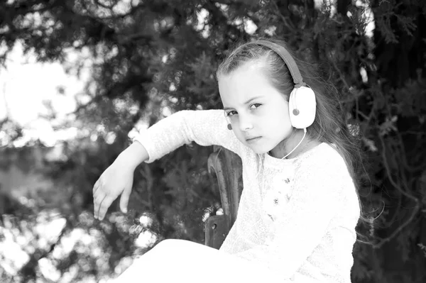 Kind Mädchen auf verträumtem Gesicht hört Musik im Freien mit Kopfhörern, Natur Hintergrund. Mädchen mit langen Haaren sitzt und genießt Musik in Kopfhörern. Kind hört friedlich oder verträumt Musik. Musikliebhaber-Konzept — Stockfoto