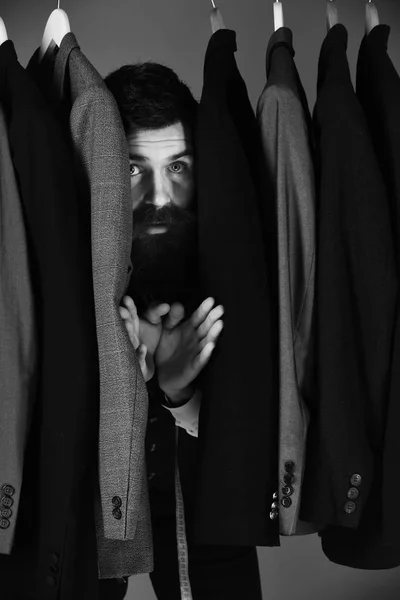 Πωλητής ή βοηθός καταστήματος κρύβεται ανάμεσα στα κοστούμια στις κρεμάστρες ρούχων — Φωτογραφία Αρχείου