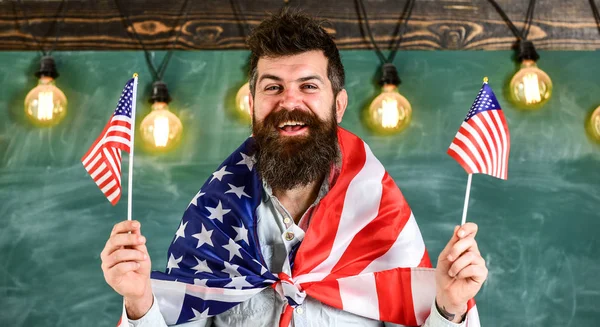 Amerikaanse leraar golven met Amerikaanse vlaggen. Man met baard en snor op blij gezicht houdt vlaggen van de VS, in de klas, schoolbord op achtergrond. Patriottische opvoeding concept. Student exchange programma — Stockfoto