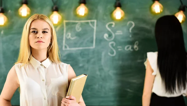 Estudiante, profesor de ropa formal en el aula. Concepto de estudiantes y aprendices. Chica se ve confiado, mientras que la señora escribiendo en el fondo de pizarra, desenfocado. Mujeres atractivas preparándose para la lección — Foto de Stock