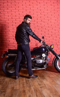 Erkeksi hobi kavramı. Yenilikçi, vahşi Motorcu deri ceket ciddi yüzüne üzerinde motosiklet üzerinde oturur. Sakallı, motorcu motorlu bisiklet garaj, tuğla duvar arka plan yakınındaki deri ceketli adam