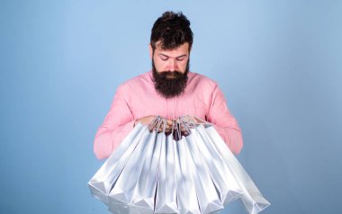 Son moda saç ve sakal gümüş çanta tutan adam. Hippi üzerinde mavi arka plan izole meraklı bakışla pembe gömlekli. Sakallı adam hediyeler, Doğum günü kutlama kavramı açılış konsantre