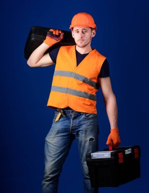 Kask, kask içinde adam araç kutusu ve araç, mavi arka plan ile bavul tutar. Donanımlı tamirci kavramı. İşçi, tamirci, tamirci, omuz araçlarıyla sakin yüz taşıdığı çanta üzerinde Oluşturucu