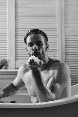 Adam banyoda tuvalet malzemeleri bulunan arka plan üzerinde köpük ile kaplı. Seks ve erotik kavramı: hurma köpük üfleme maço