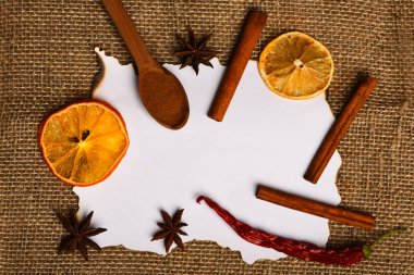 Tarçın, kurutulmuş portakal ve biber, anasonu boş kağıt, tarifi, kopya alanı çevresinde. Çul arka plan üzerinde kağıt parçası. Mutfak tarifi kavramı. Baharat kaşıkla beyaz kağıt yatıyordu
