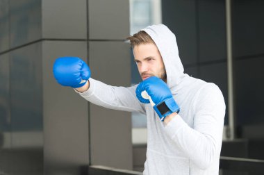 Adam atlet spor ile konsantre yüzündeki pratik boks yumruk, kentsel arka plan eldiven. Onun boks becerileri eğitim. Boksör hood baş uygulamaları yumruk yumruk. Sporcu boxer eğitim boks eldivenleri