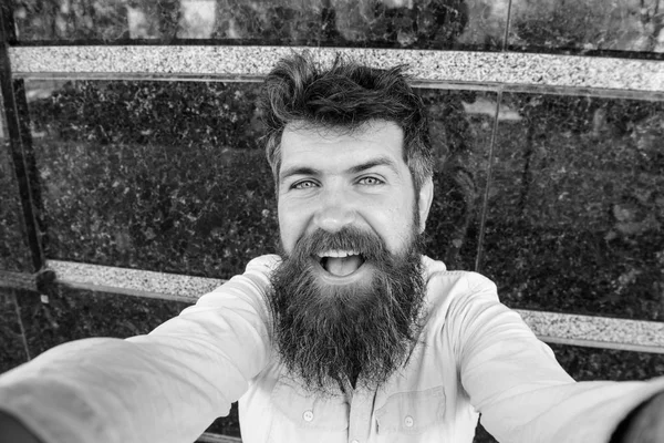 Adam, sakal ve bıyık neşeli, gülümseyen yüzünde siyah mermer zemin üzerine turist. Hippi, turist tousled saçlı ve uzun sakal kameraya, seyir selfie fotoğraf çekiyorum. Vlogging kavramı. — Stok fotoğraf
