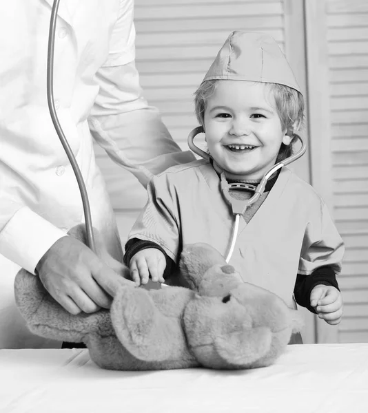 Mutlu yüz ile oğlu doktor çalıyor. Sağlık ve çocukluk kavramı küçük yardımcısı oyuncak ayı inceliyor. Ayı erkek el tutar — Stok fotoğraf