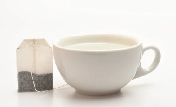 Mug filled with boiling water and teabag on white background. Cup or white porcelain mug with transparent hot water and dry bag of tea near. Process of tea brewing in ceramic mug. Tea time concept — Stock Photo, Image