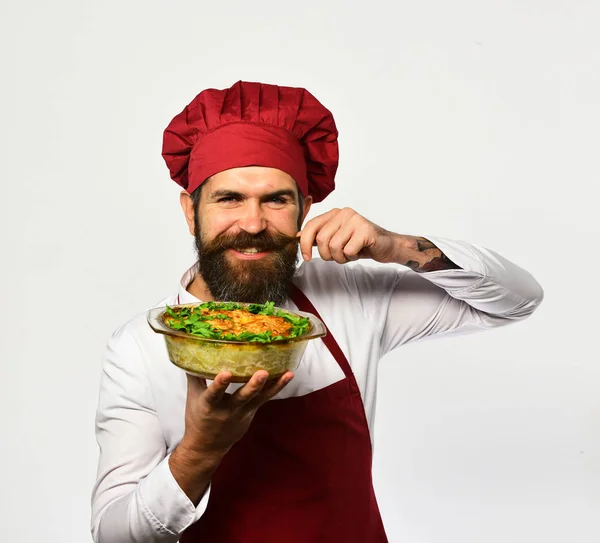 Cook with flirty face in burgundy uniform holds baked dish