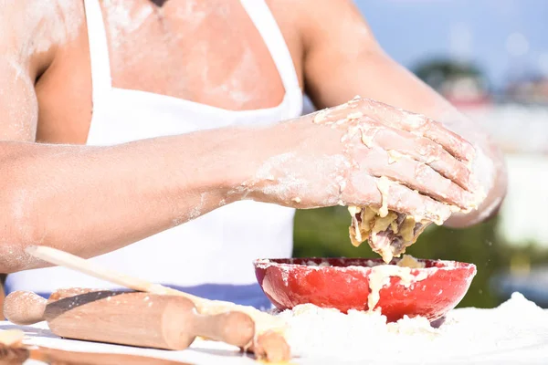 Mãos de padeiro muscular ou cozinhar massa de amassar na tigela. Mãos de chef cozinheiro trabalhando com massa e farinha. Tigela com massa, rolo e farinha espalhados por toda parte, de perto. Conceito de padaria — Fotografia de Stock