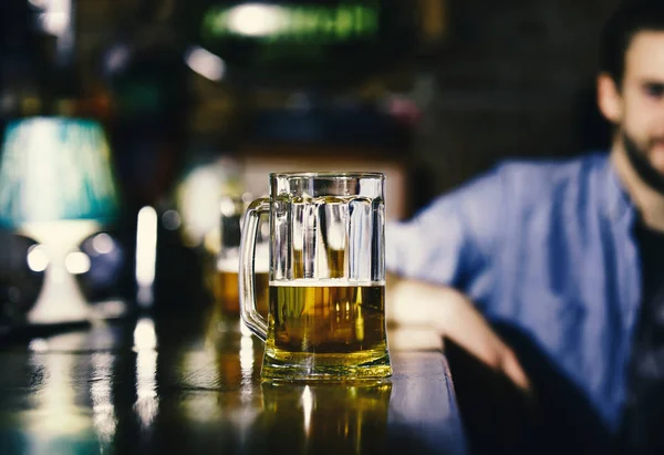 Copo de cerveja no balcão de madeira. Homem senta-se atrás de vidro de cerveja leve . — Fotografia de Stock