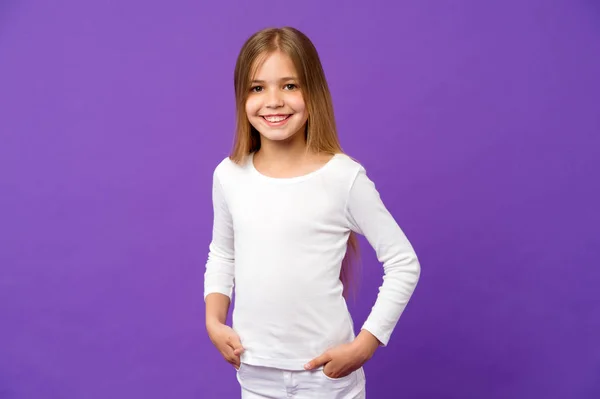 小さな女の子は、紫色の背景に笑顔します。紫色の背景に長いブロンドの髪と笑顔の子。カジュアル シャツの子供モデル。ファッションのスタイルと傾向。幸せな子供時代と保育 — ストック写真