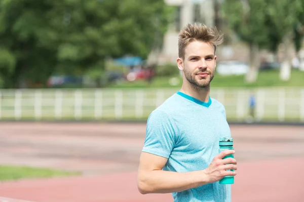 Staying hydrated. Man athletic appearance holds water bottle keep staying hydrated during training. Guy sport clothes refreshing. Athlete cares body hydration after training at stadium sunny day