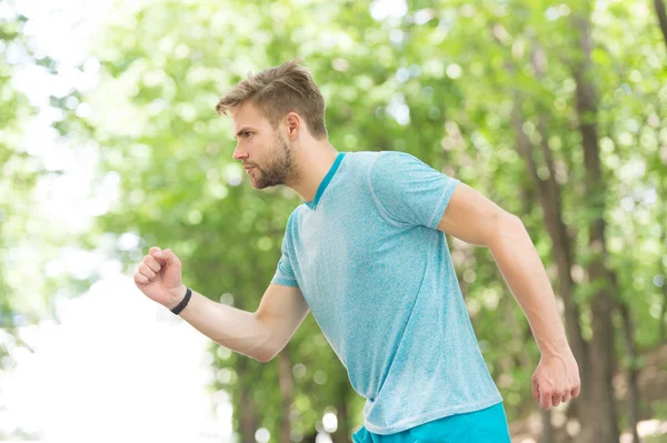 Pasando a su meta. Hombre joven confiado corriendo en el parque, vista lateral. El deportista se mueve ambiciosamente para lograr el objetivo deportivo. Concepto de masculinidad y logros deportivos. Guy concentrado corre por su objetivo — Foto de Stock