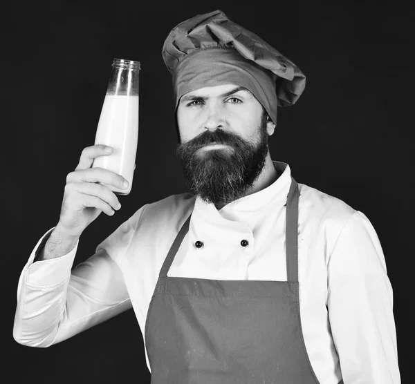 Kock med milkshake eller yoghurt. Mannen med skägg innehar glasflaska på svart bakgrund — Stockfoto