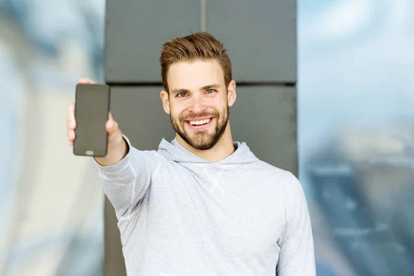 Showing his brand new smart phone. Man beard with smartphone, urban background. Man with beard happy smiling face shows smartphone. Guy cheerful demonstrates new gadget. Mobile gadget concept