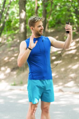 Seni gördüğüme çok sevindim. Çalıştırmadan önce atlet cep telefonu video seslenmek. Adam atlet gülümseyen yüz çevrimiçi eğitim koç, Doğa arka plan bakın. Adım sayar ve kulaklık ile sporcu online video eğitim