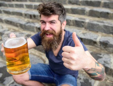 Sakal ve bıyık tutan cam bira ve gösterileri başparmak yukarı, taş merdivenle arka plan ile olan adam. Fıçı bira kavramı. Bira, seçici odak birlikte olan adam. Hipster neşeli yüz bira içiyor
