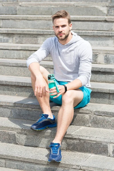 Working out on stairs. Man athletic appearance holds water bottle. Man athlete sport clothes refreshing. Sport and healthy lifestyle concept. Athlete drink water training at stadium sunny day