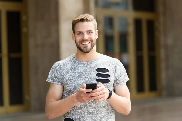 Staying in touch. Send message concept. Man with beard walks with smartphone, urban background. Guy use smartphone to send message stay in touch. Man typing text message smartphone