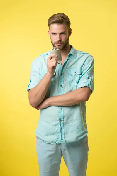 Man confident face recommends perfume, yellow background. Guy with bristle holds bottle perfume, enjoy fragrance. Male fragrance concept. Man holds bottle perfume enjoy pleasant aroma