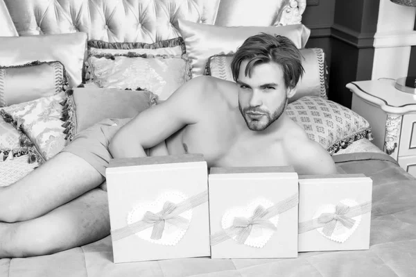 Hombre con las cajas de regalo se encuentran en la cama en el dormitorio — Foto de Stock