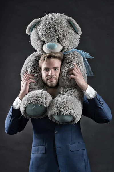 I am so sorry. Man carries giant teddy bear on neck, dark background. Reunion gift concept. Guy calm bearded face with toy teddy bear as gesture of reunion or apology. Man formal suit regrets quarrel