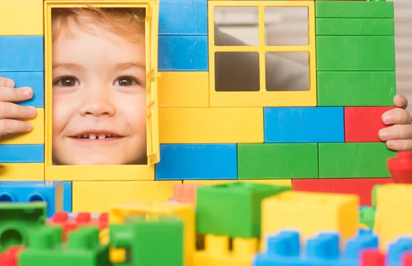 Niño juega con ladrillos de construcción, mirando a través de la puerta de juguete — Foto de Stock