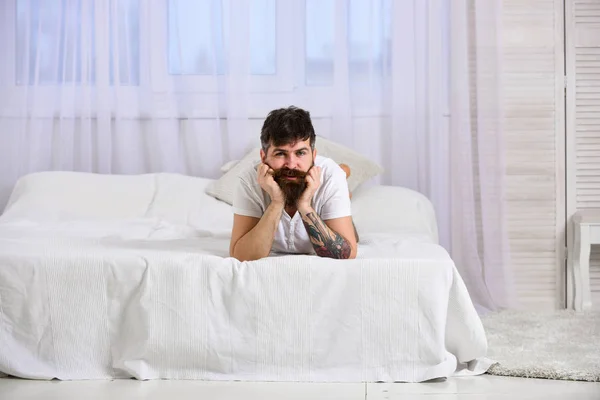 Adam sakin yüz beyaz çarşaf yatağa kenarında döşeme. Adam arka plan üzerinde beyaz perde yatak, döşeme. Yatak odası ve yatak kavramı. Maço sakal ve bıyık rahatlatıcı, dinlenme. — Stok fotoğraf