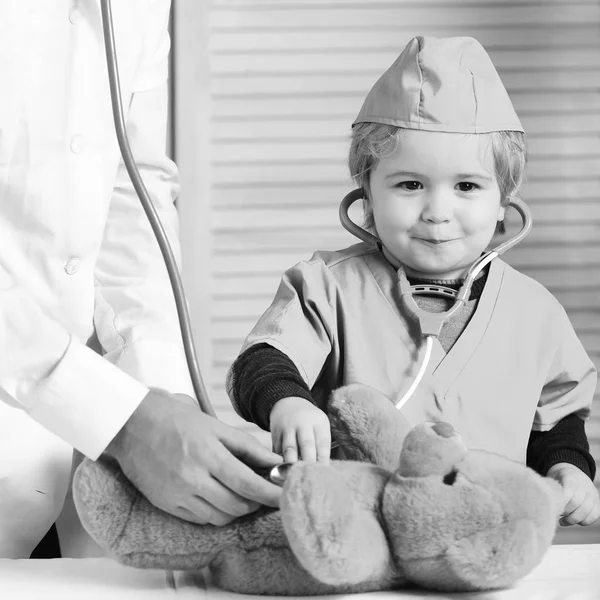 Criança com rosto sorridente joga médico Saúde e conceito de infância. Pequeno assistente examina ursinho de pelúcia . — Fotografia de Stock