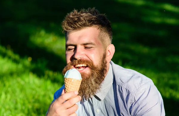 Concept de tentation. Homme barbu avec un cône de crème glacée. Homme avec barbe et moustache sur le visage heureux profiter de crème glacée, herbe sur fond, déconcentré. Homme à longue barbe mange de la crème glacée, tandis que s'assoit sur l'herbe — Photo