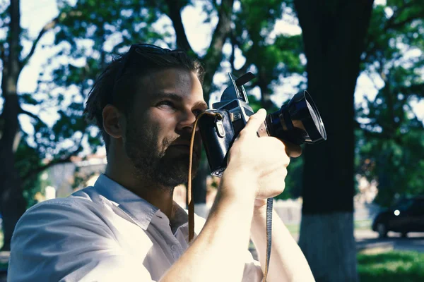 Photographer holds retro camera with big lense. Man with beard holds photocamera on green park background — Stock Photo, Image