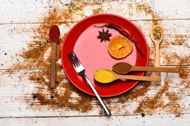 Mutfak konsepti. Baharat öğütülmüş kırmızı biber ve curcuma toz olarak dağılmış. Baharat tüm ahşap yüzey üzerinde dağınık. Tabak ve çatal Beyaz ahşap zemin üzerinde kurutulmuş portakal ve serin biber ile