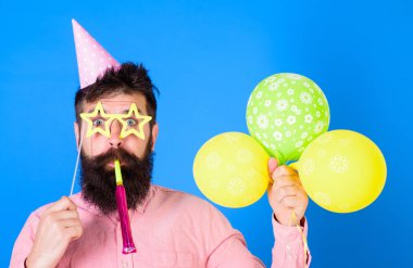 Sürpriz yüzündeki sakallı adam hava balonları, mavi arka plan tutar. Tatil öznitelikleri ile parti şapkalı adamı kutluyor. Hipster Star gözlük darbeler parti boynuz şeklinde. Sürpriz kavramı
