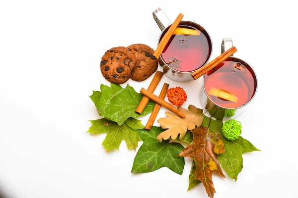 Canecas com vinho quente ou bebida quente perto de folhas de outono e biscoitos no fundo branco, de perto. Conceito de bebida quente. Vinho amassado ou bebida quente em canecas de metal com paus de canela — Fotografia de Stock