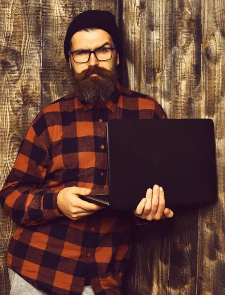 Brutalne kaukaski poważne zarośnięty hipster elektrowni fotowoltaicznej w czerwony czarny kraciaste koszule z kapelusz i okulary na tle brązowy vintage drewniane studio. — Zdjęcie stockowe